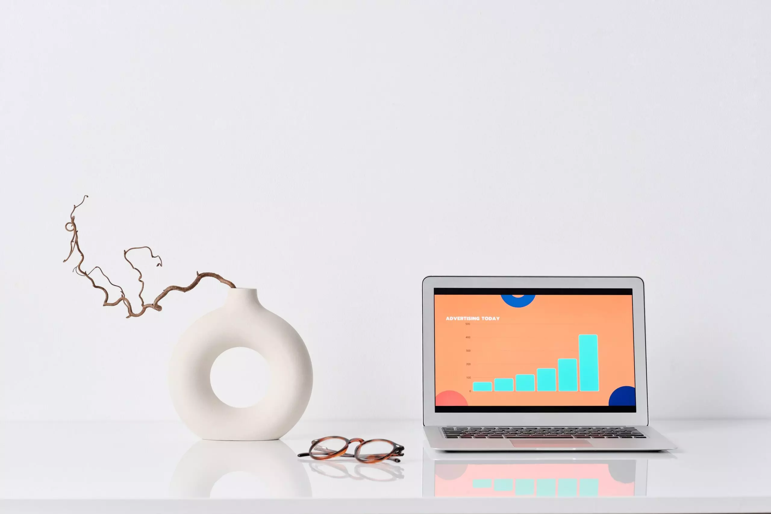 Desk with with a laptop with digital marketing results, a vase, and glasses