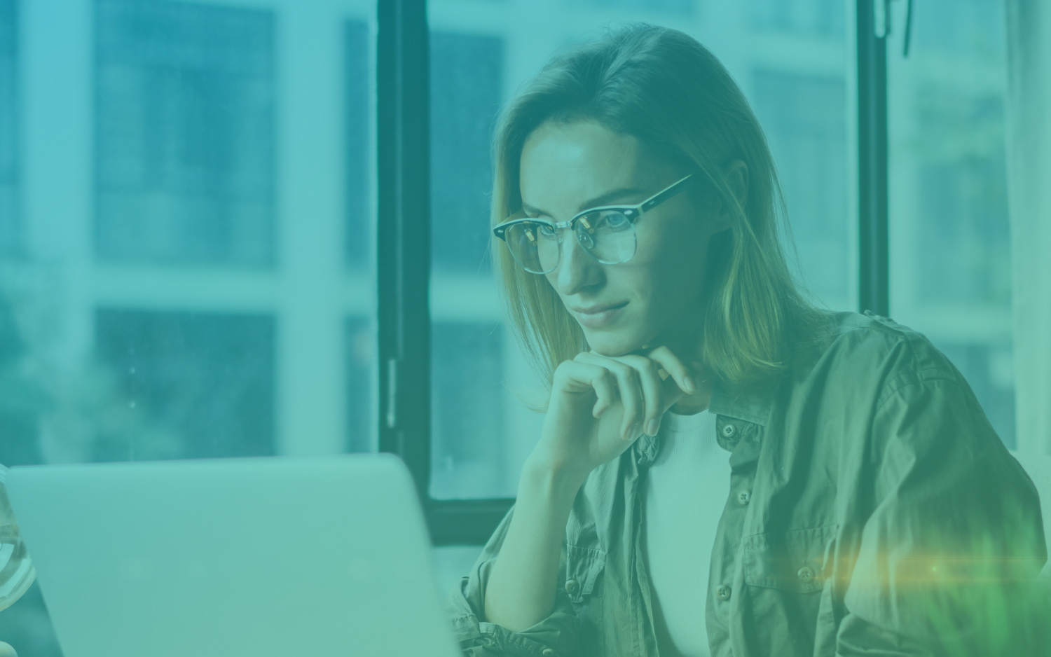 woman with blonde hair wearing glasses working on her laptop in front of some windows